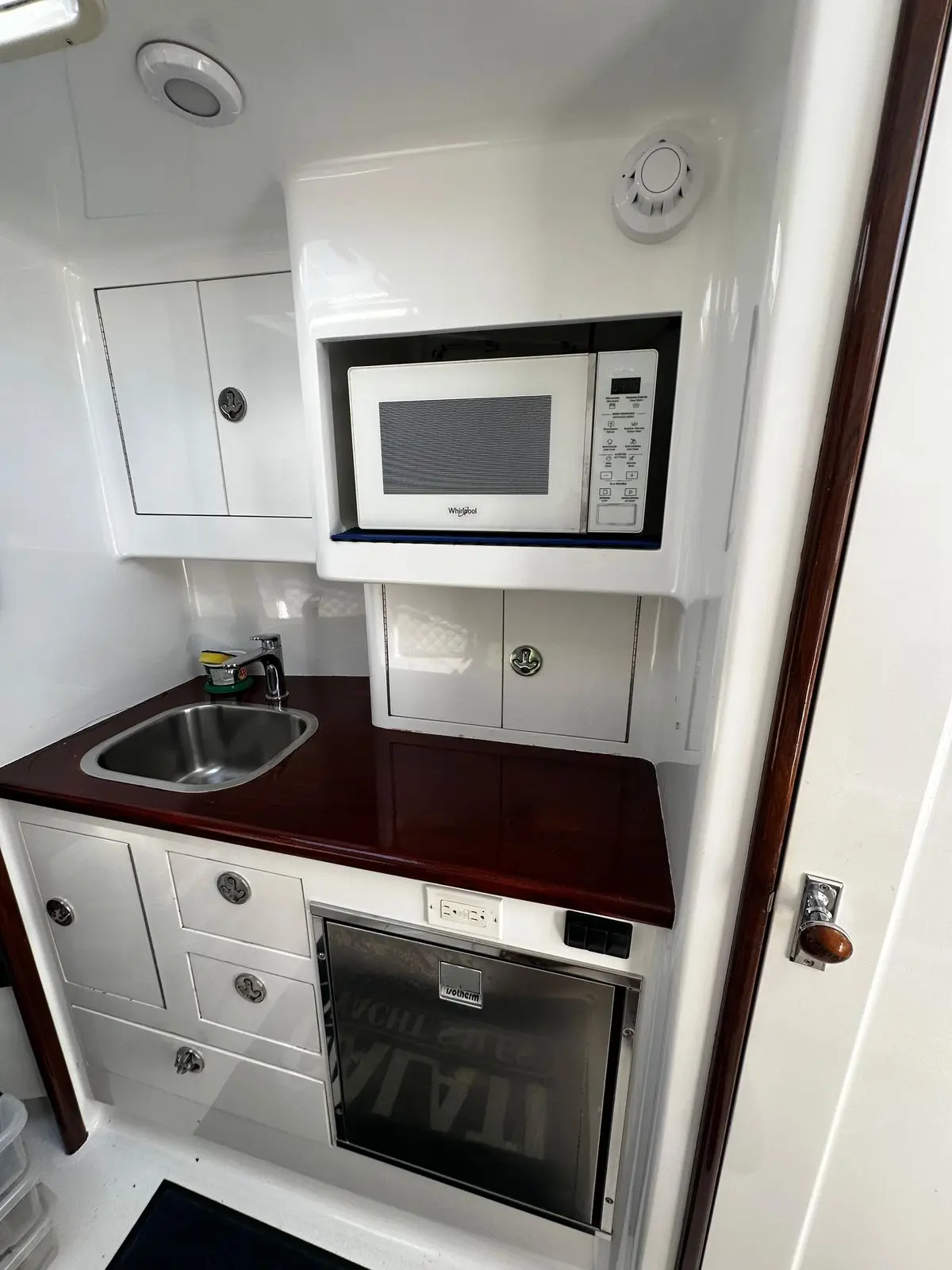 Sportfishing boat galley with a microwave, sink and dark wood countertop above white cabinets