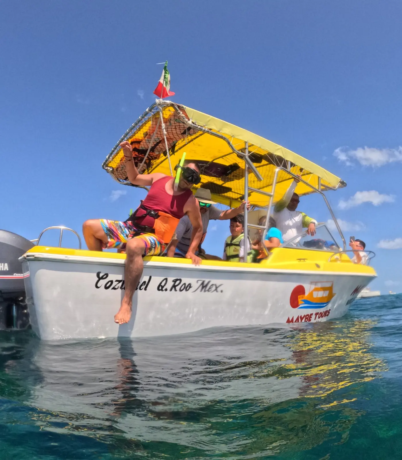 Speedboat with a yellow canopy and a Mexican flag floating in calm water off Cozumel with guests aboard
