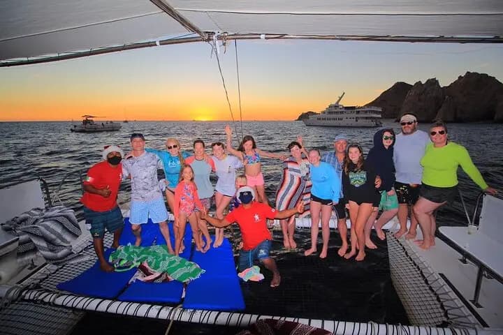 Group of adults and kids posing on a catamaran's net deck at sunset near the Land's End rocks