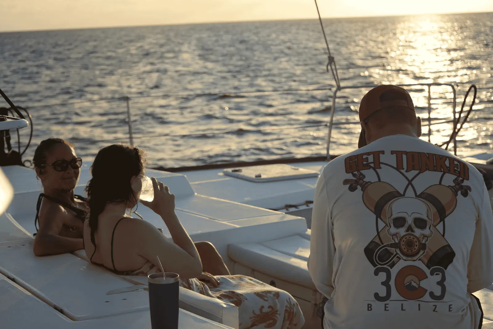 Guests lounging on a catamaran deck as the low sun glitters on the sea off Belize