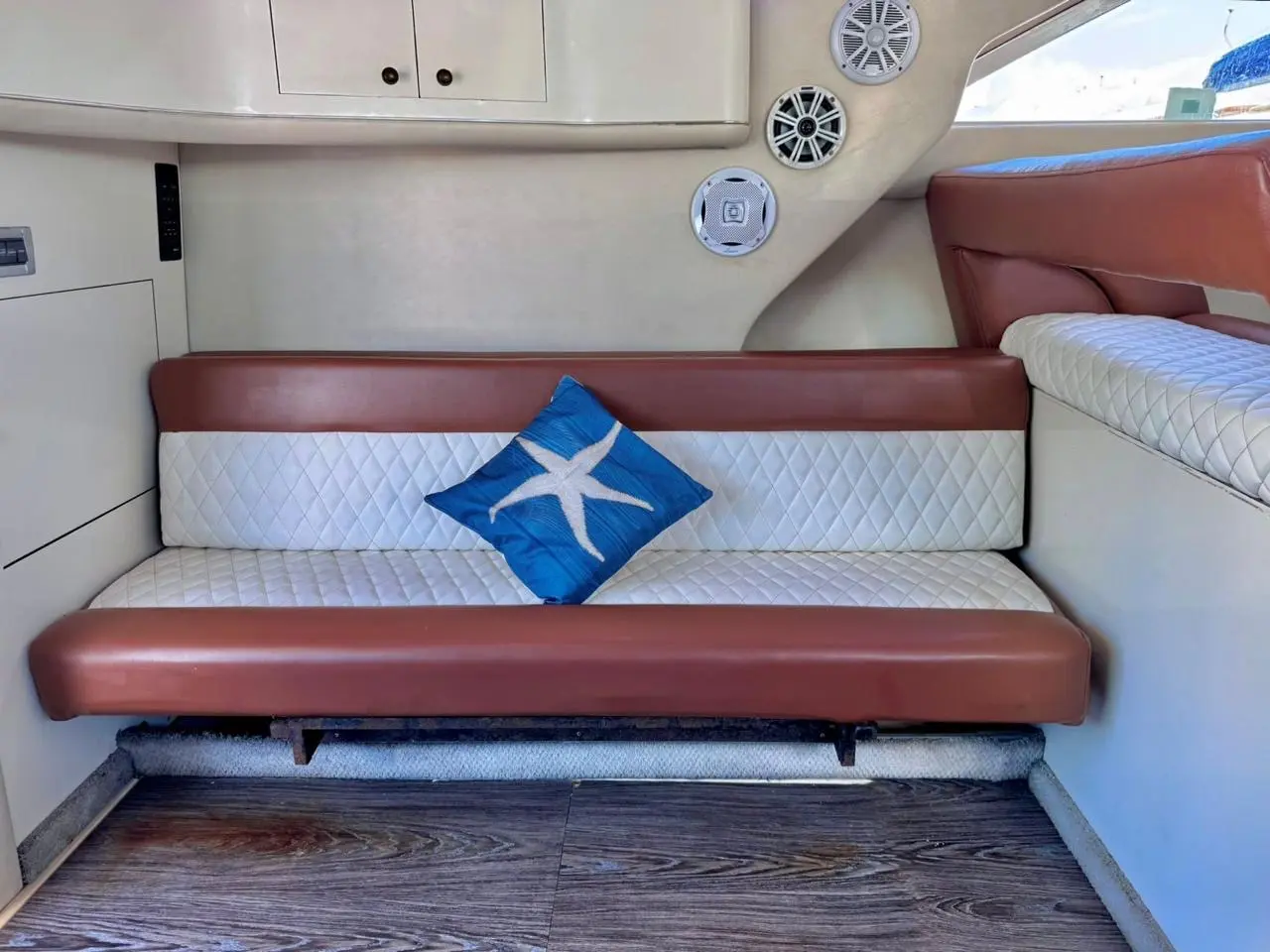 Brown and cream quilted leather settee with a blue starfish pillow inside a yacht cabin