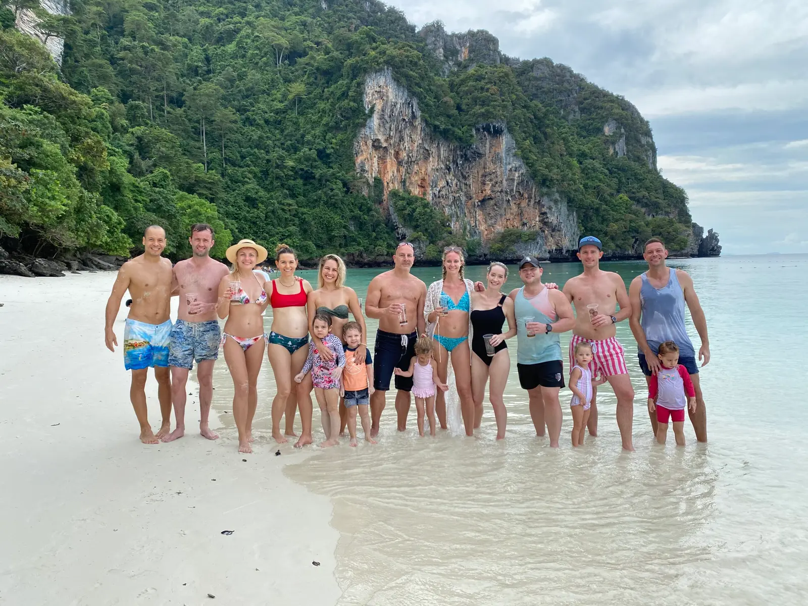 Adults and kids lined up for a group shot in the shallows of a white-sand beach in the Phi Phi Islands