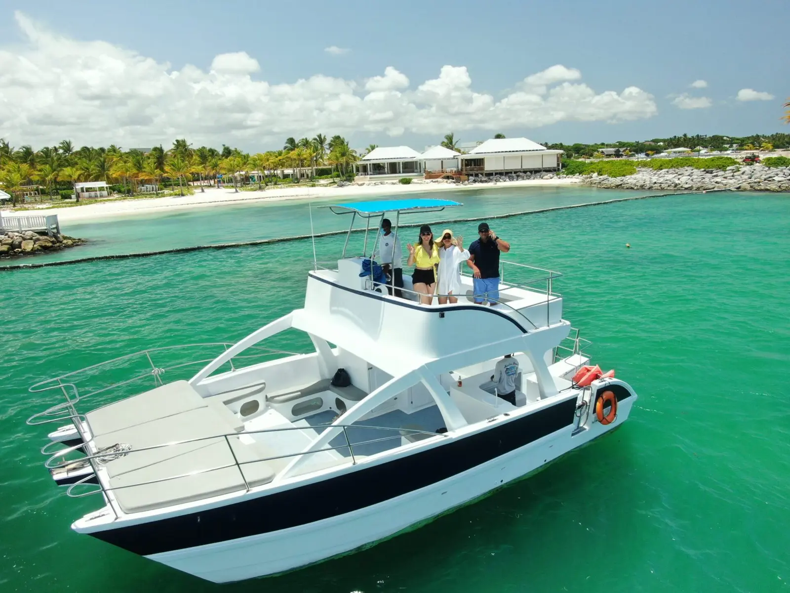 Guests stand on the flybridge of a power catamaran near a palm-lined resort shore in Cap Cana