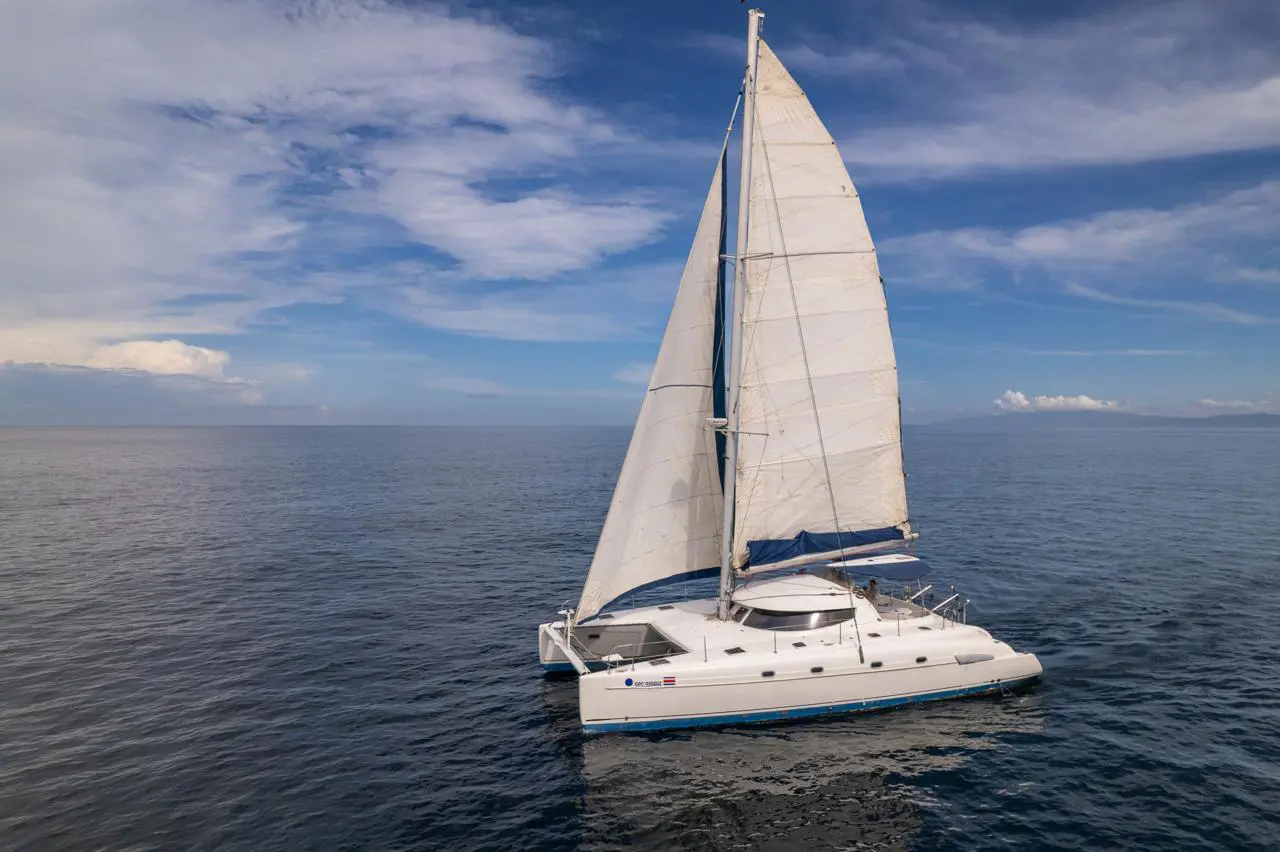 Bow-on view of a sailing catamaran gliding over glassy open water under scattered clouds in Costa Rica
