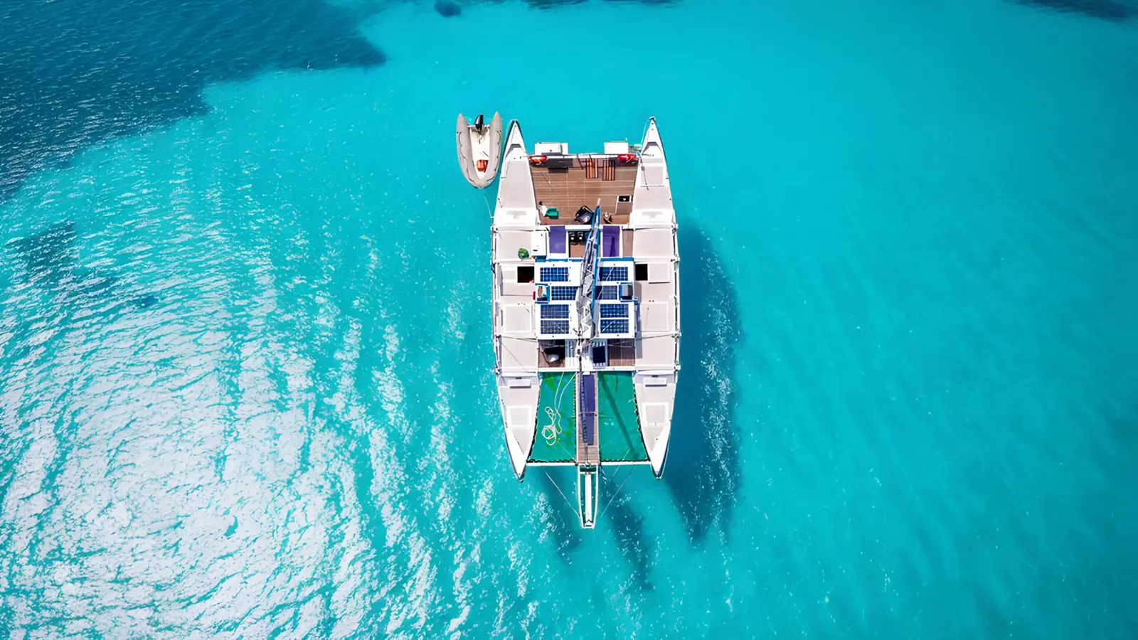 Overhead view of a catamaran with a small tender at its stern on clear turquoise water off Zanzibar
