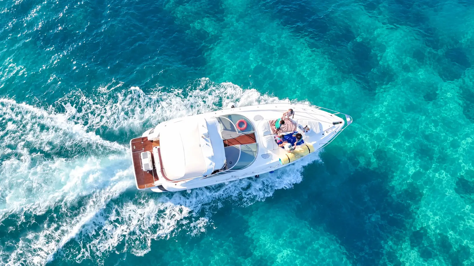 Overhead drone shot of an express cruiser with guests on the bow, carving a wake over reef water