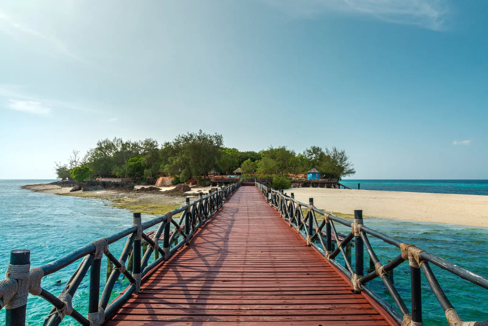 Wooden jetty with rope railings stretching over turquoise water to Prison Island