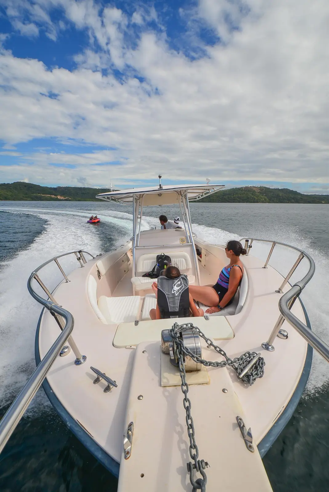 Two guests relaxing on the bow seats of a center console boat cruising past green Costa Rica hills