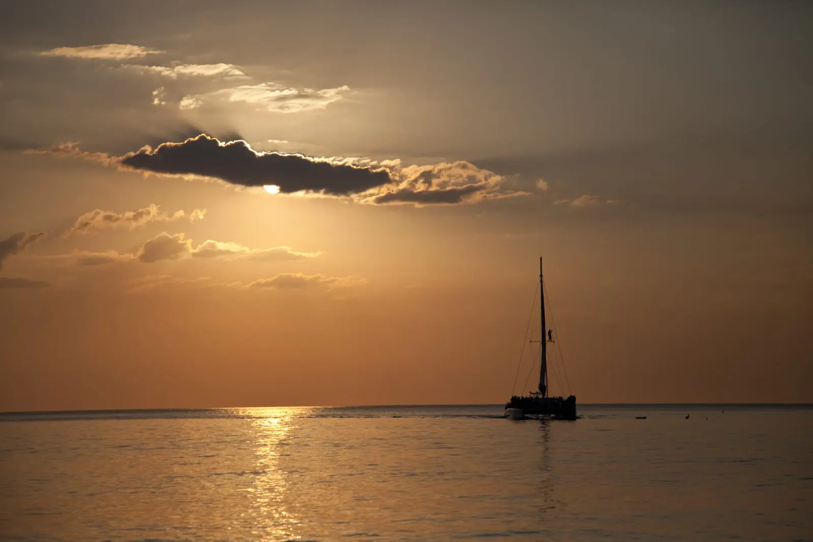Distant sailing catamaran silhouetted on the horizon under a hazy golden sky off Montego Bay