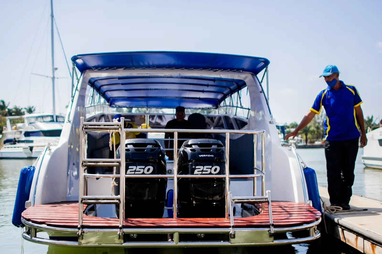 Stern of a speedboat with twin outboard engines and a swim ladder as a crew member waits on the dock