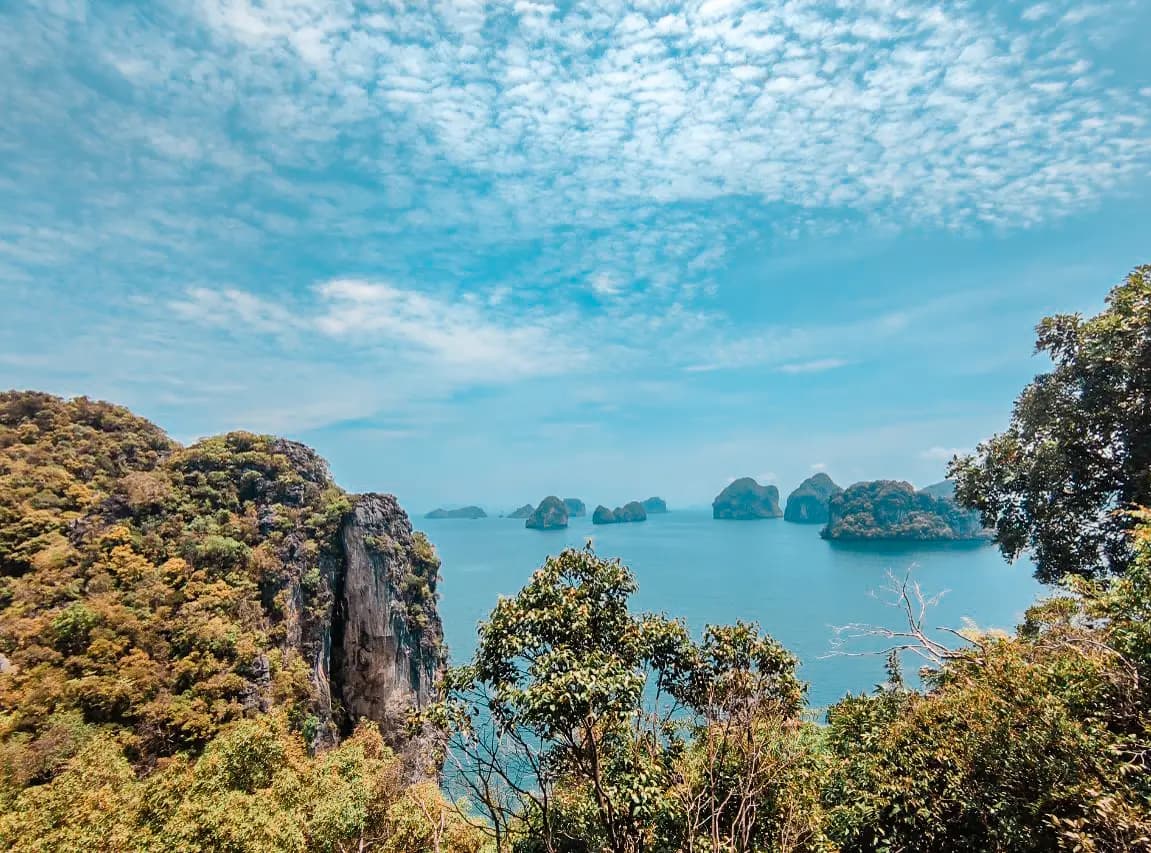 Jagged karst peak and distant limestone islets under a dappled sky, seen from a hilltop in Krabi