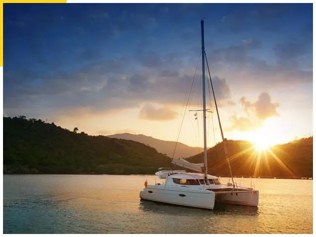Sailing catamaran anchored in a calm bay as the sun sets behind forested hills in Costa Rica