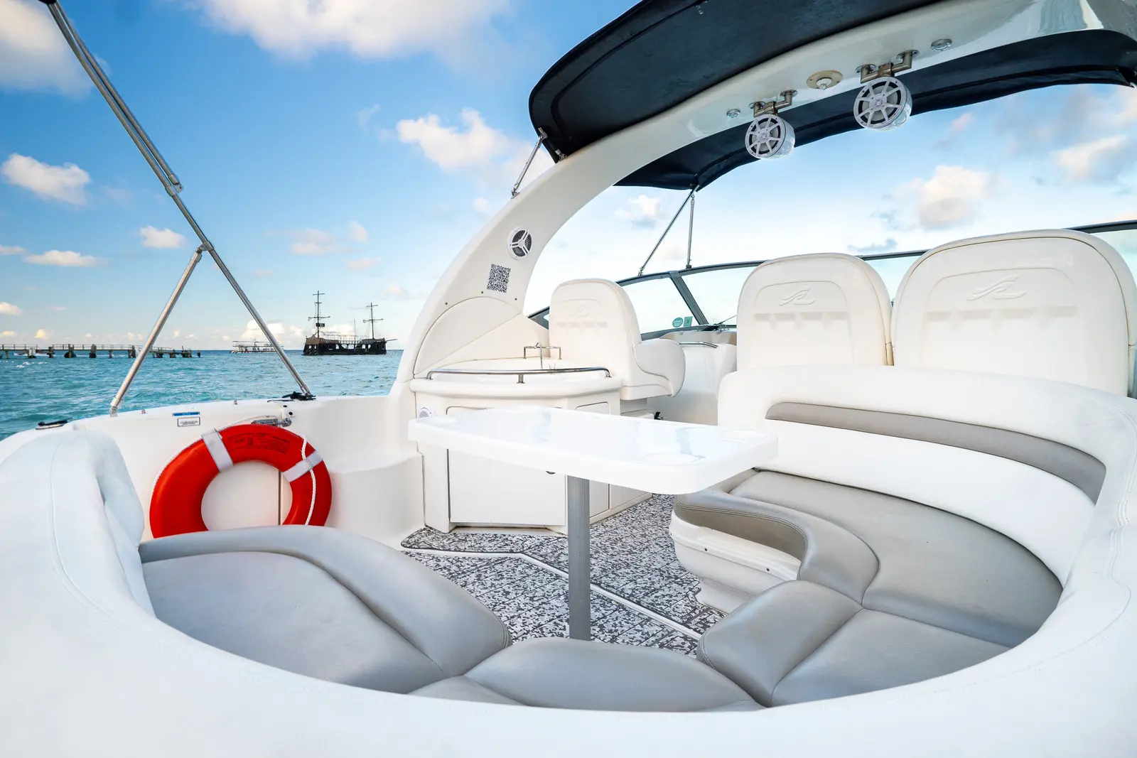 Motor yacht cockpit with wraparound seating, a life ring and table, a tall ship on the horizon