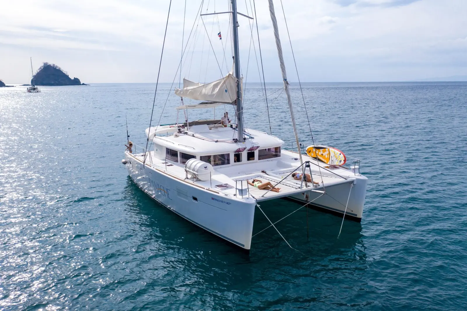 Sailing catamaran at anchor off Costa Rica, with a rocky islet and a sailboat on the horizon