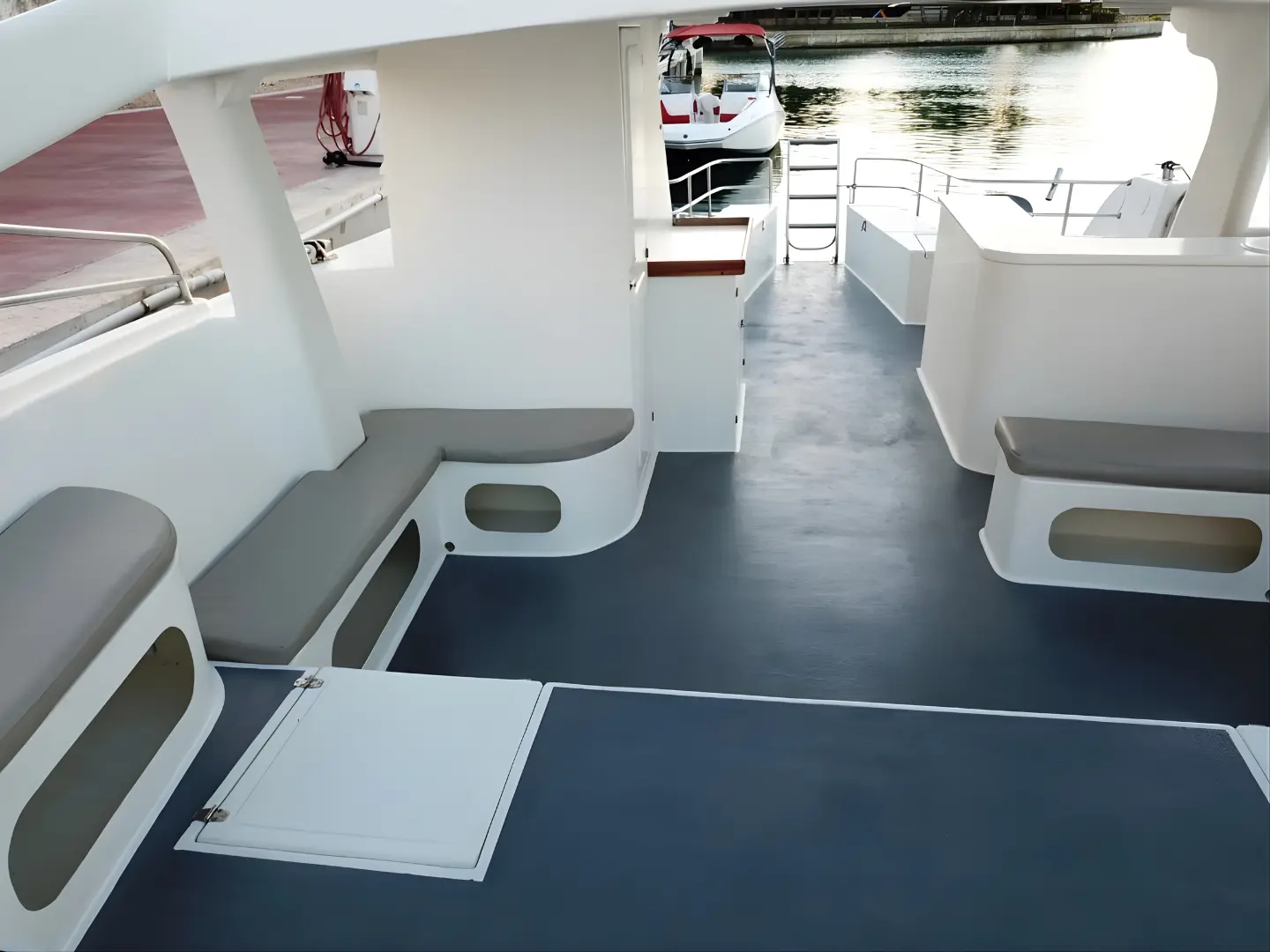 Open deck of the power catamaran with gray cushioned benches and stairs up to the top deck