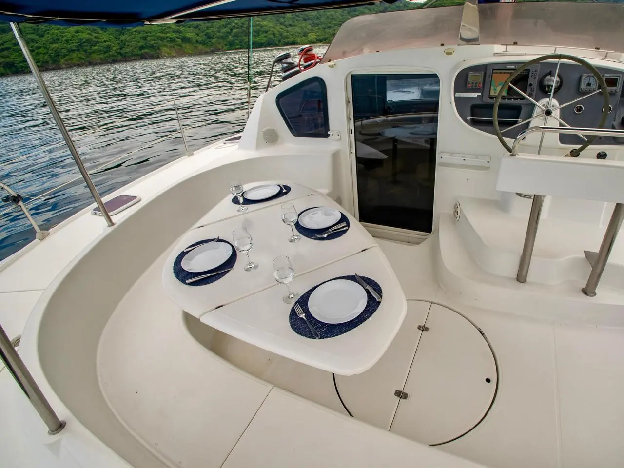 Cockpit table set for four with navy placemats beside the helm wheel of a sailing catamaran