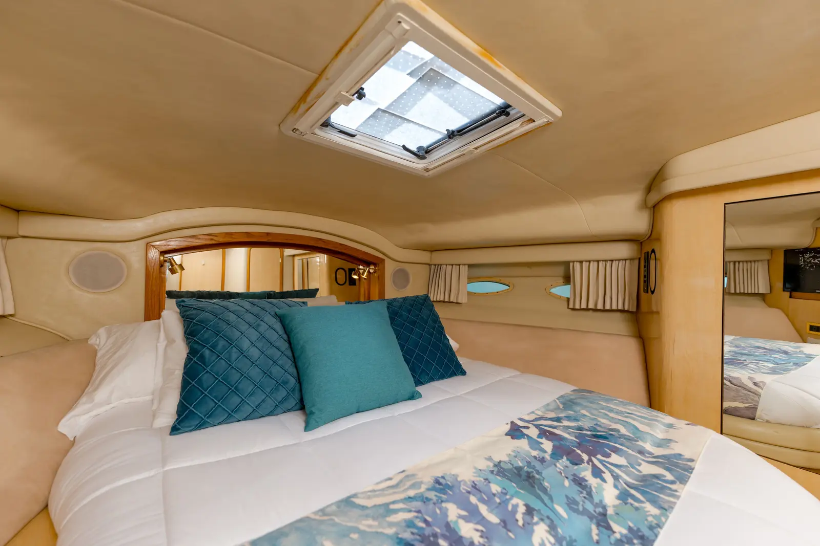 Yacht master cabin with a double bed, teal cushions and an overhead skylight hatch