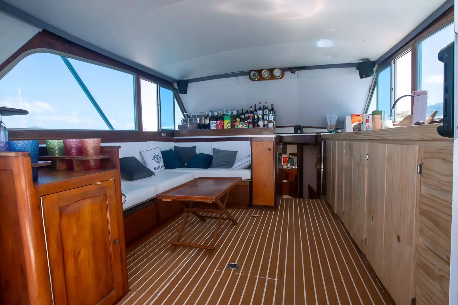 Teak-floored saloon of the sportfishing boat with a cushioned sofa, folding table and bar shelf