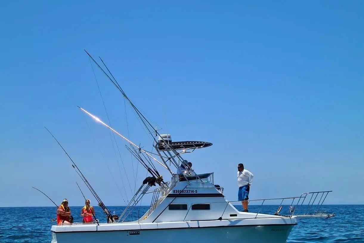 Sportfishing boat with outriggers up and anglers on deck cruising the blue water off Los Cabos
