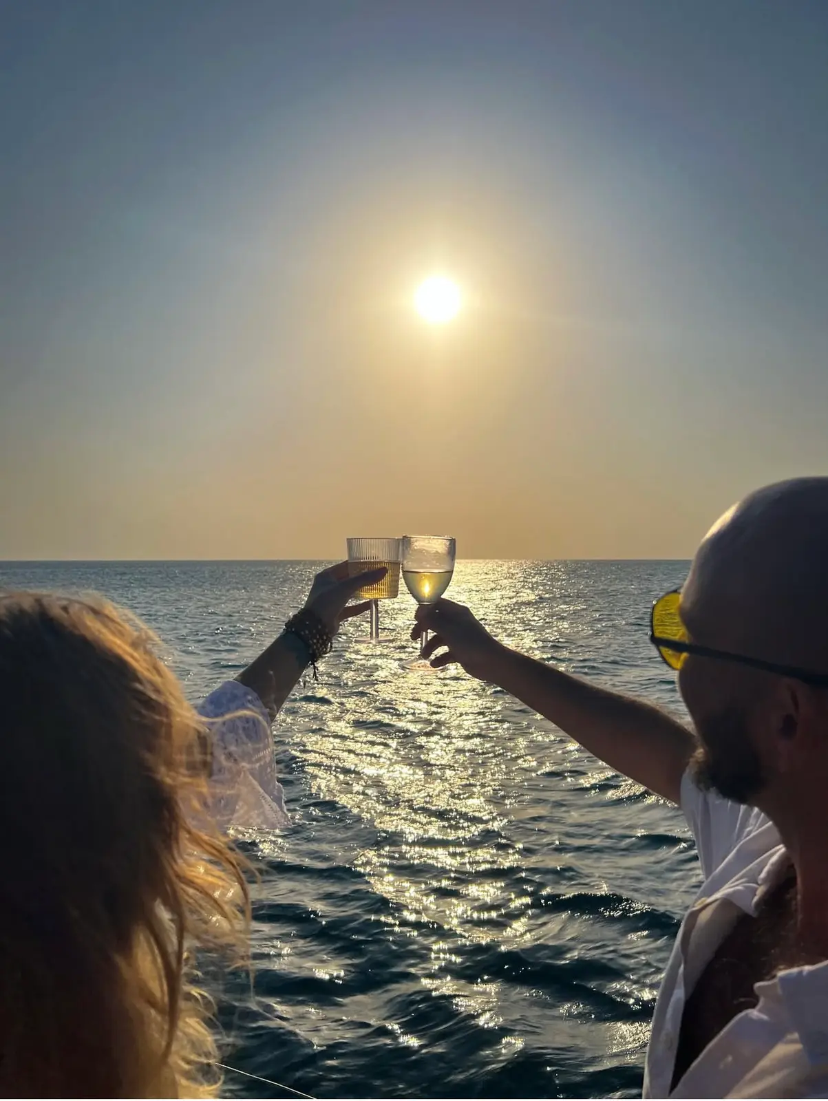Two guests raising glasses toward the low sun over the glittering sea off Zanzibar