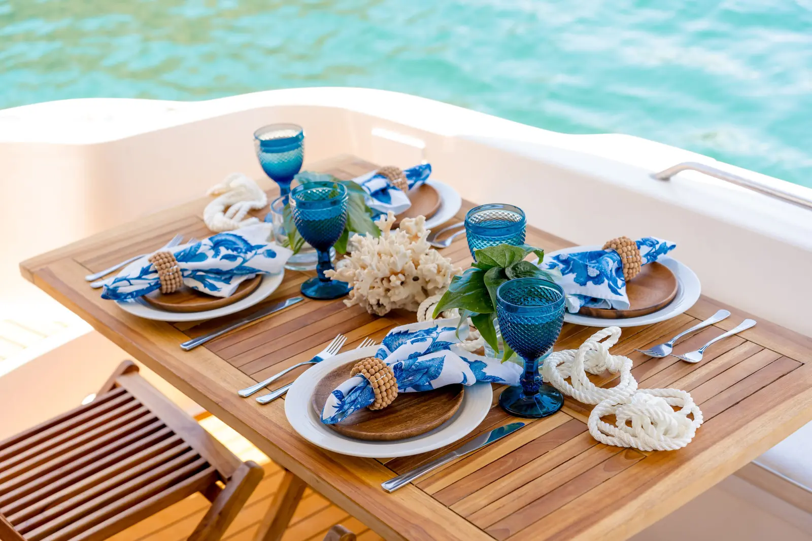 Teak deck table set with blue glassware, patterned napkins and a coral centerpiece aboard the yacht