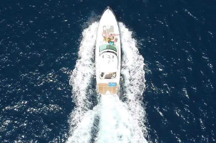 Overhead drone view of a motor yacht leaving a white wake across deep blue water off Cabo San Lucas
