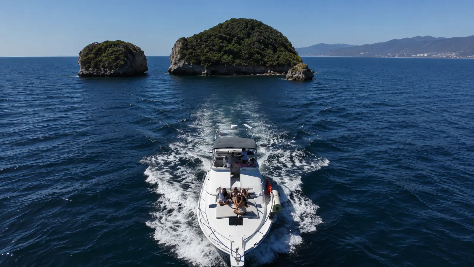 A white flybridge yacht speeds toward two green rocky islets across deep blue Banderas Bay