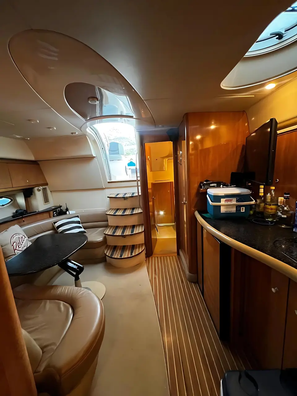 Yacht salon with curved leather seating, a dining table and wood cabinets leading to the bow cabin
