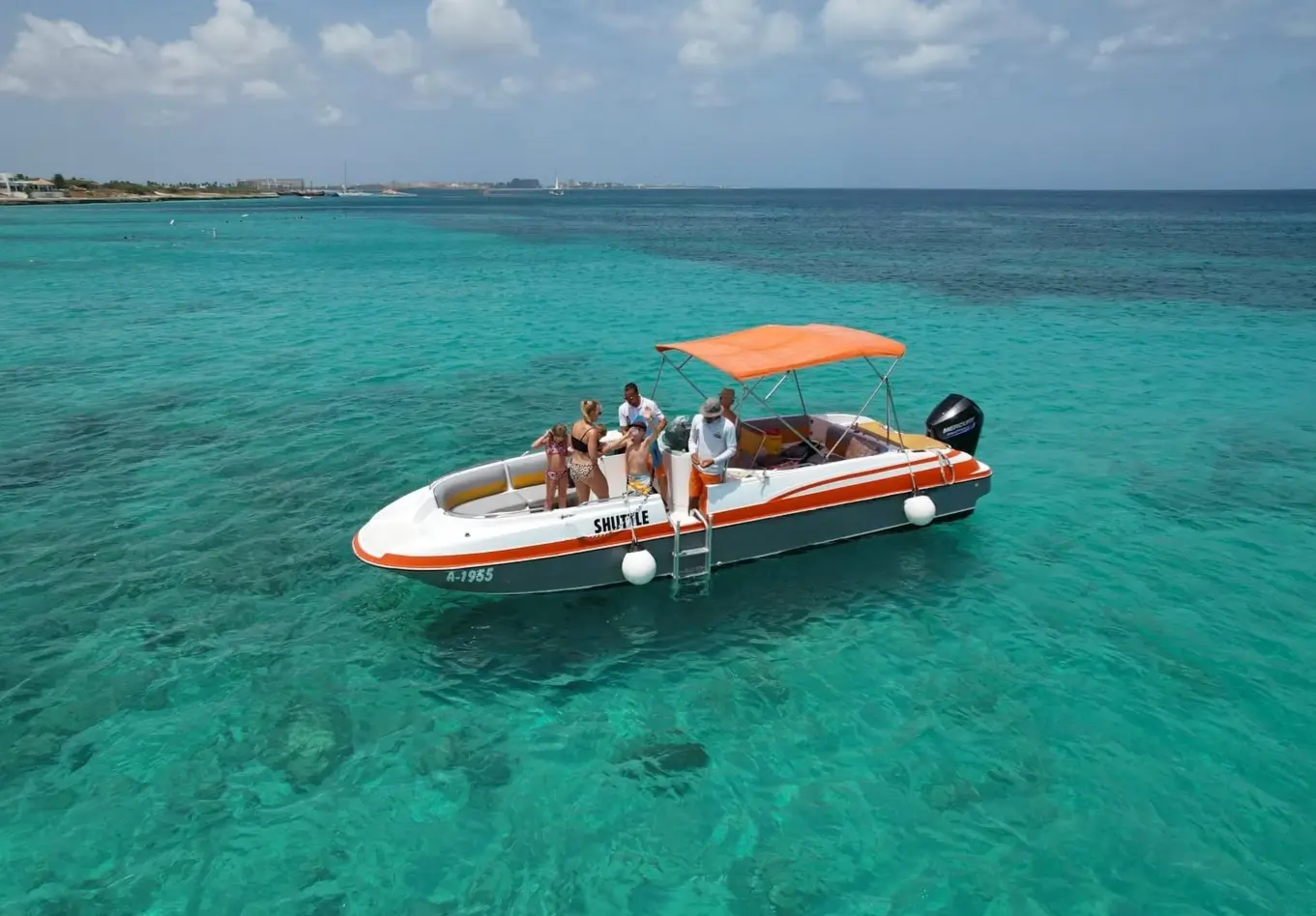 Guests aboard a deck boat with an orange canopy anchored in clear turquoise shallows off Aruba