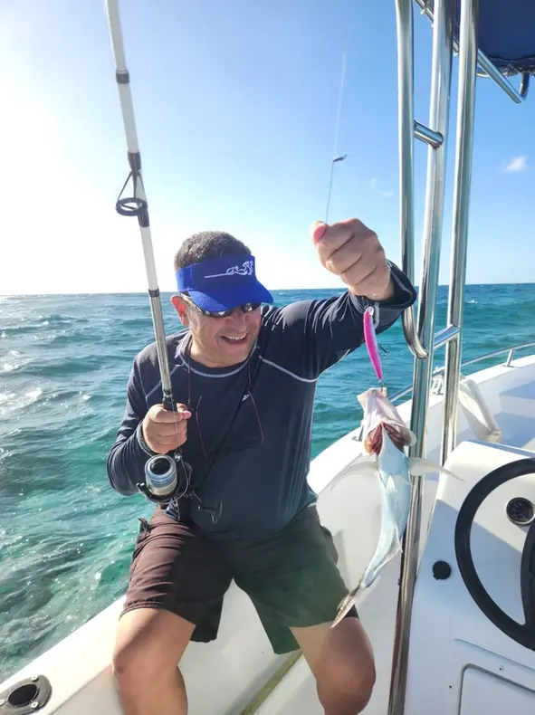Smiling angler in a visor lifting a small catch on his line aboard a center-console fishing boat