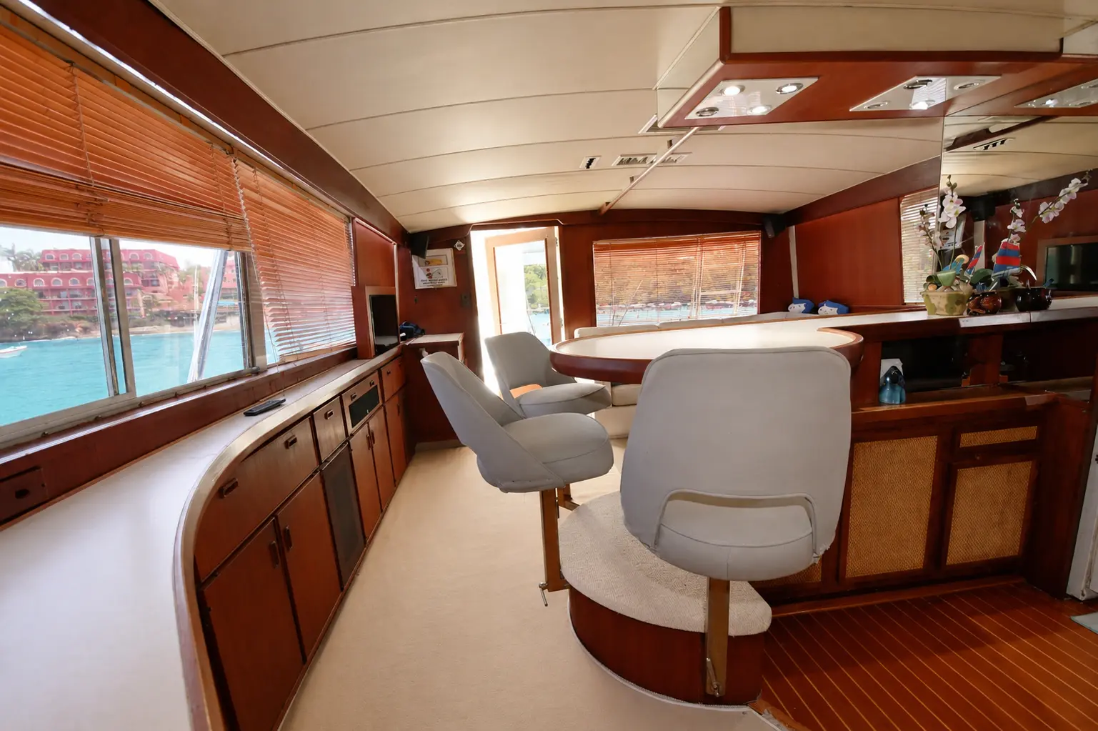 Salon of a sportfishing boat with white swivel chairs, a wood-trimmed counter and wide windows