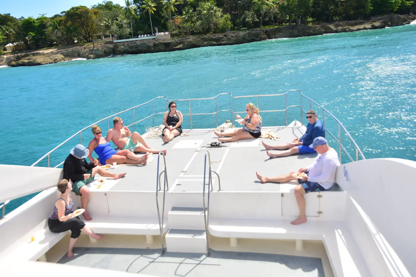 Guests sunbathing on the bow deck of a catamaran cruising past the palm-lined Puerto Plata coast