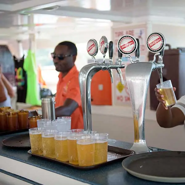 A bartender pouring draft beer into rows of cups at the catamaran's onboard bar