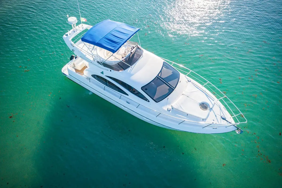 Aerial view of a white flybridge yacht with a blue canopy anchored in clear turquoise Riviera Maya water