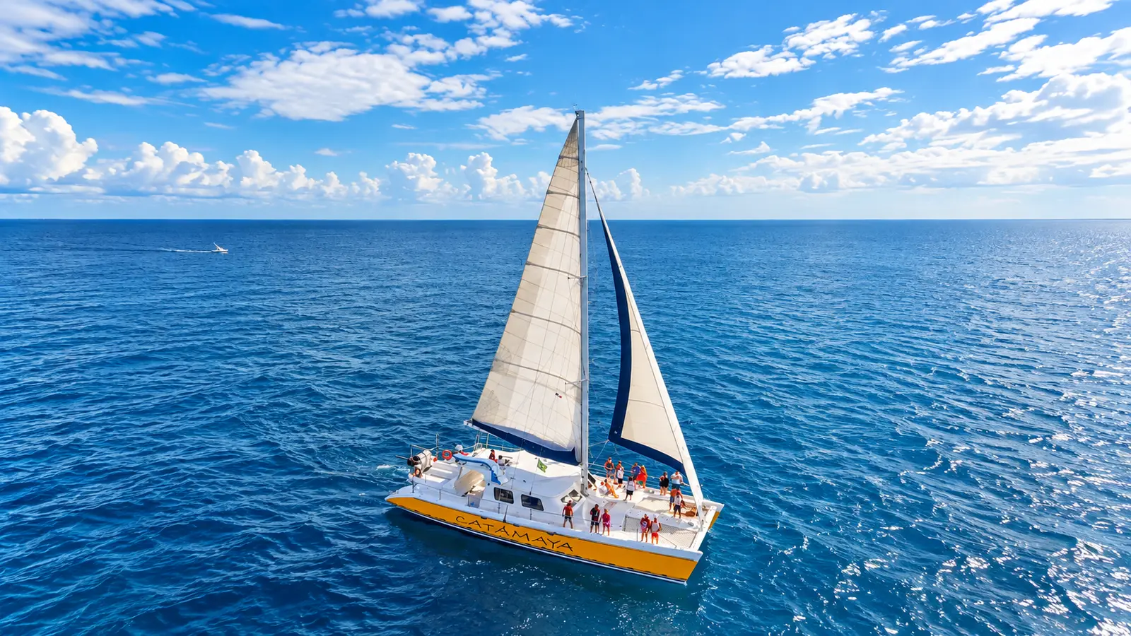 Yellow sailing catamaran with guests aboard crossing the open Riviera Maya sea under full sail