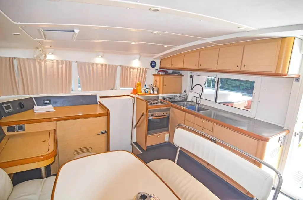 Power catamaran salon with a wood-trimmed galley, stove and cream-cushioned dining area