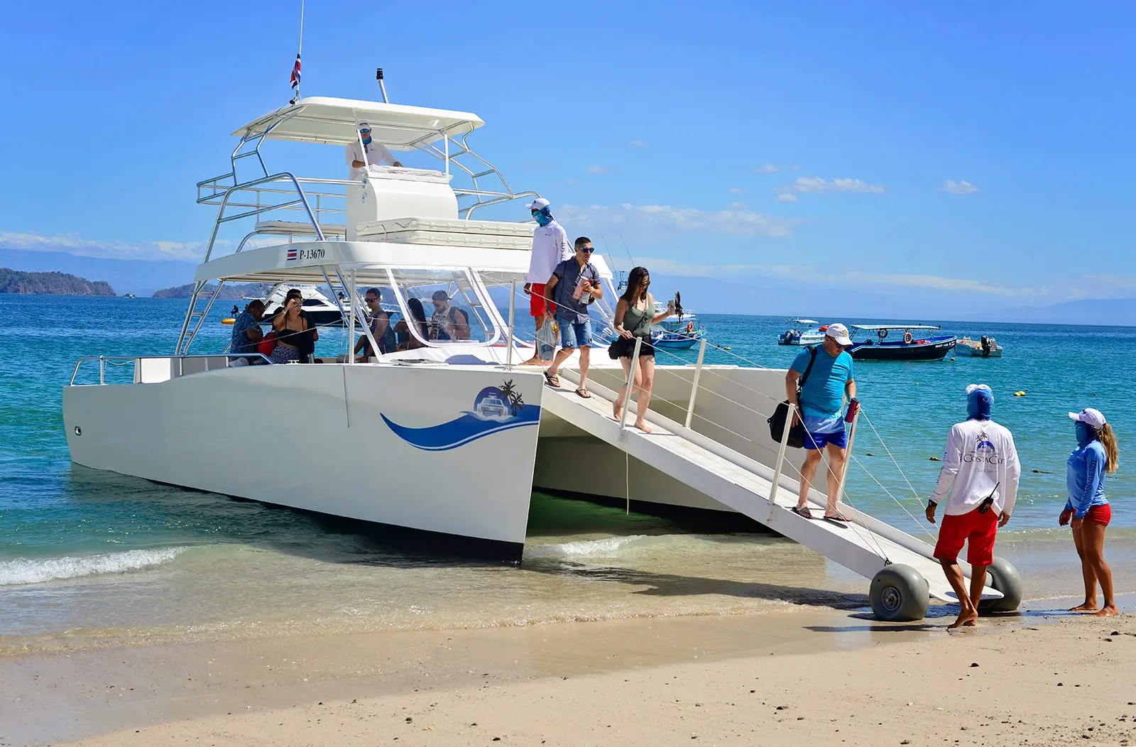 Catamaran with its boarding ramp lowered onto a Tortuga Island beach as guests and crew come ashore