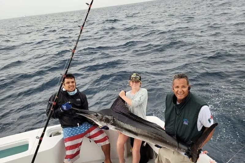 Three anglers holding up a large billfish on the deck of a sportfishing yacht
