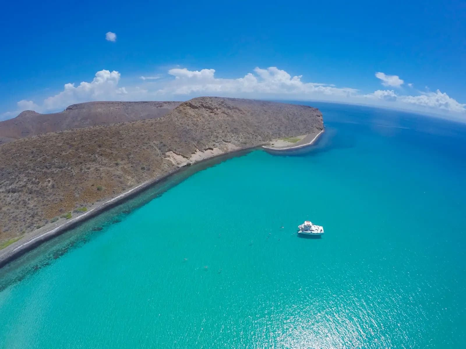Aerial view of a boat anchored in a turquoise bay beside a long desert peninsula near La Paz