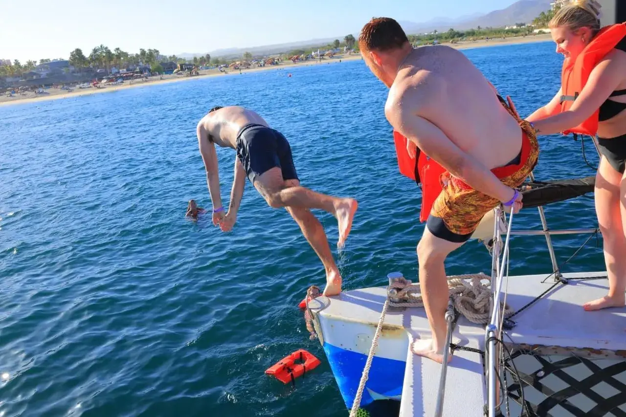 Guest diving headfirst off a catamaran's bow into Los Cabos waters as others in life vests wait their turn