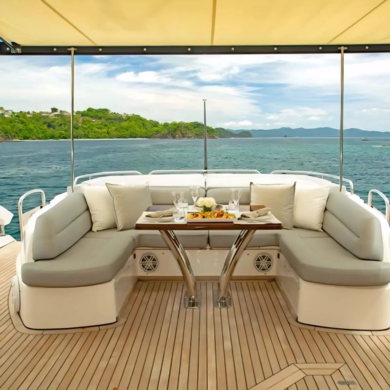 Shaded deck lounge with a U-shaped cream sofa and teak table looking out to green islands off Guanacaste