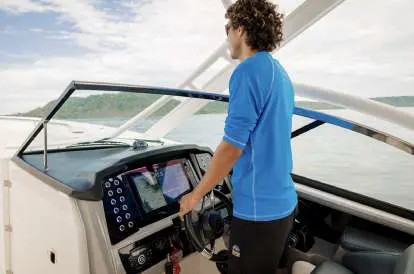 A man in a blue rash guard steers the center-console boat from its touchscreen helm
