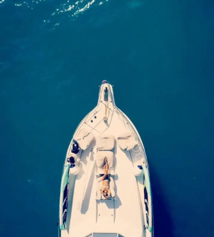 Top-down view of a guest sunbathing on the bow of a motor yacht surrounded by deep blue water