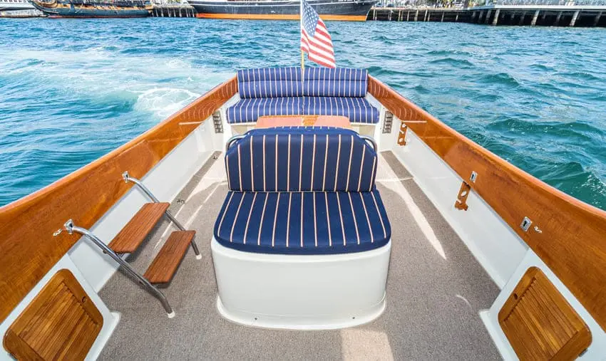 Aft deck of a picnic boat with navy-and-white striped seats and teak steps, a flag flying over the wake