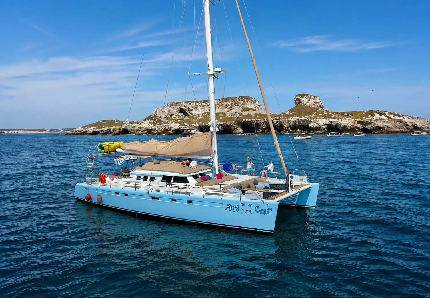 A light blue sailing catamaran at rest beside rocky islets off Puerto Vallarta under a clear sky