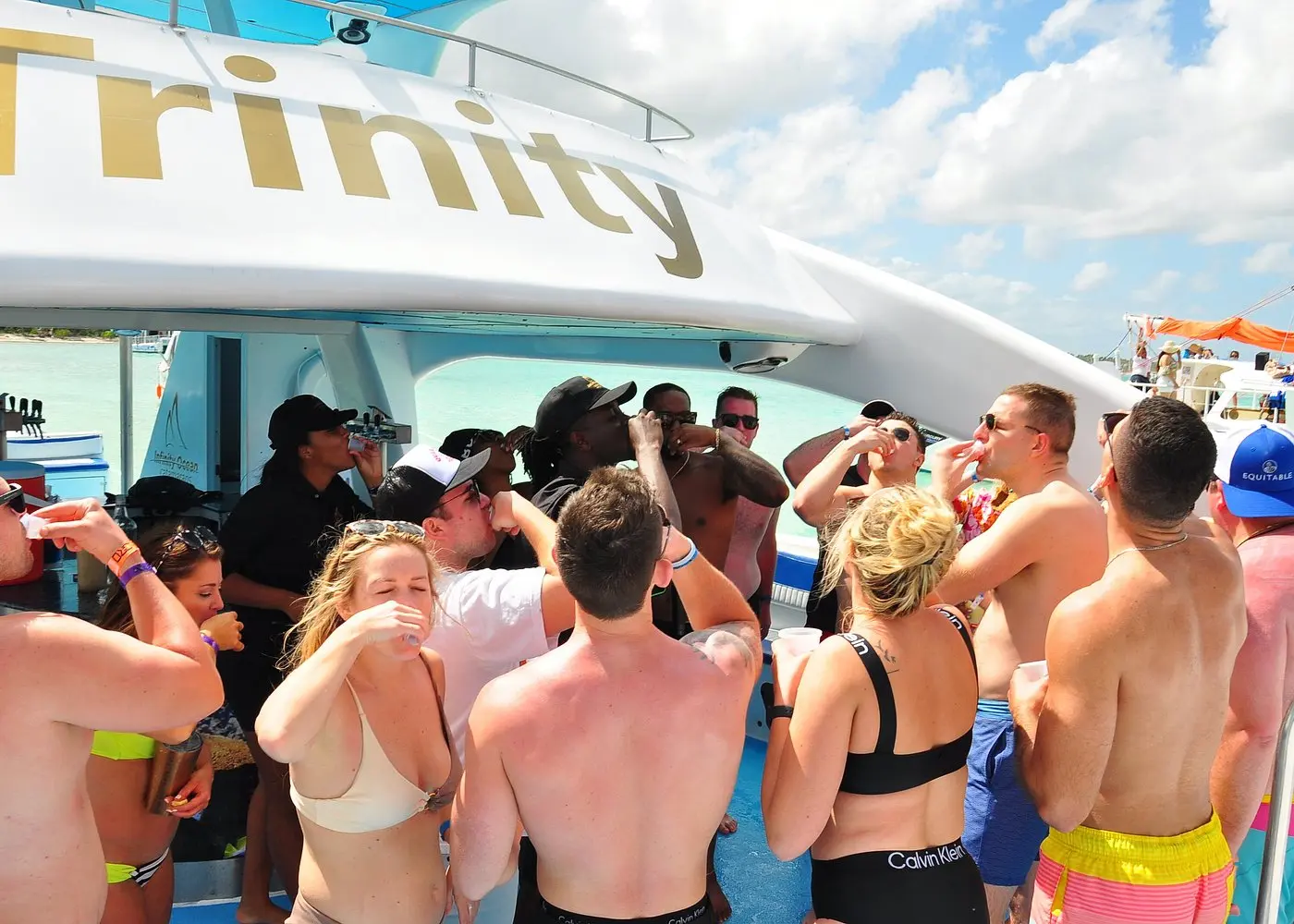 Guests in swimwear knocking back drinks together beneath the catamaran's upper deck