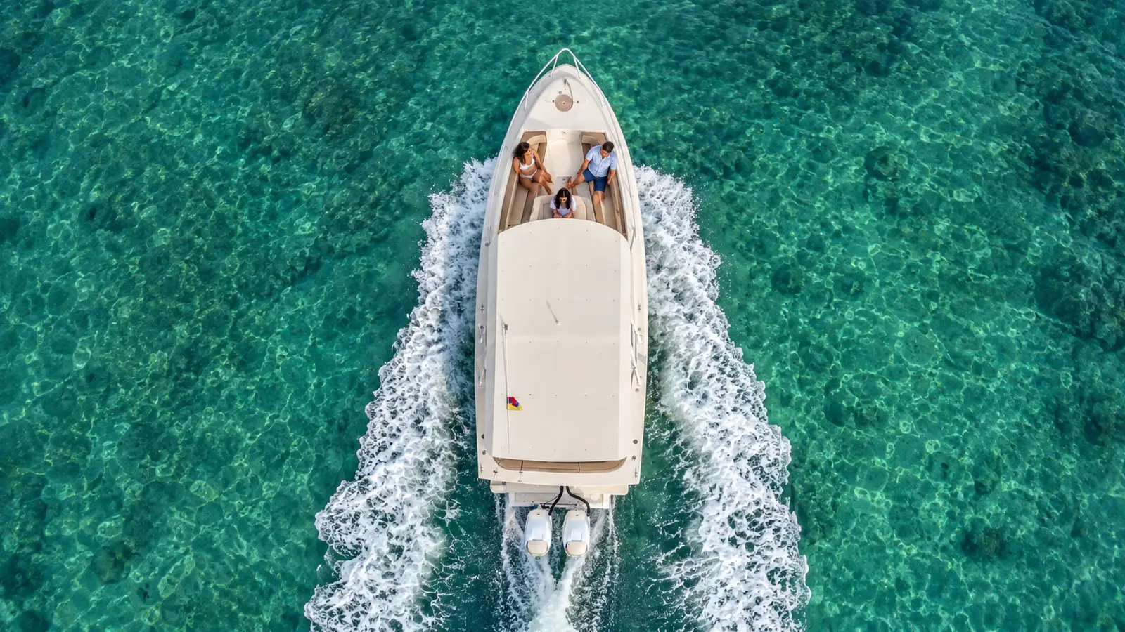 Overhead view of a speedboat racing over clear emerald water in the Rosario Islands, guests on the bow