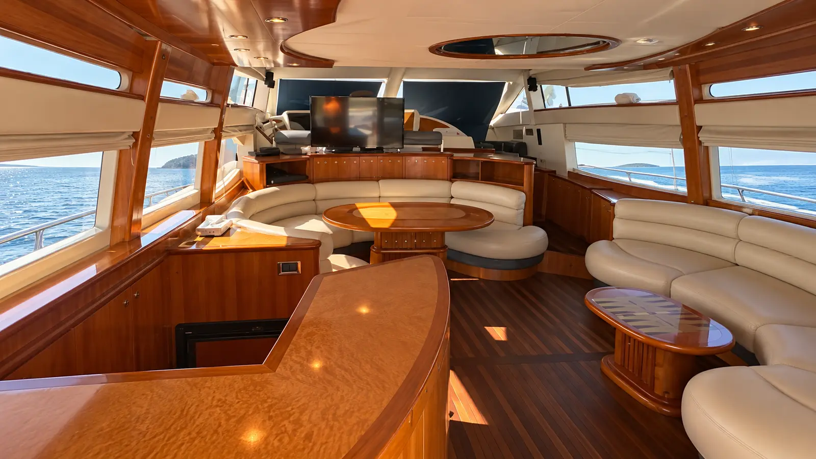 Yacht salon with glossy wood paneling, cream leather sofas and a curved wooden bar