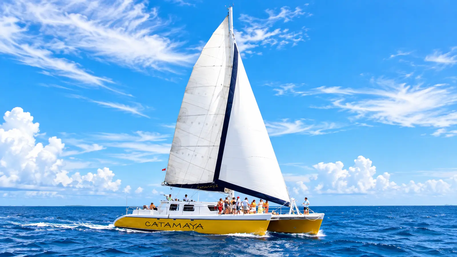 Yellow-hulled sailing catamaran under full sail with guests aboard on deep blue water off the Riviera Maya
