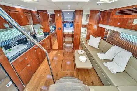Yacht salon with a long cream sofa, glossy wood cabinetry and a galley set with glasses and champagne